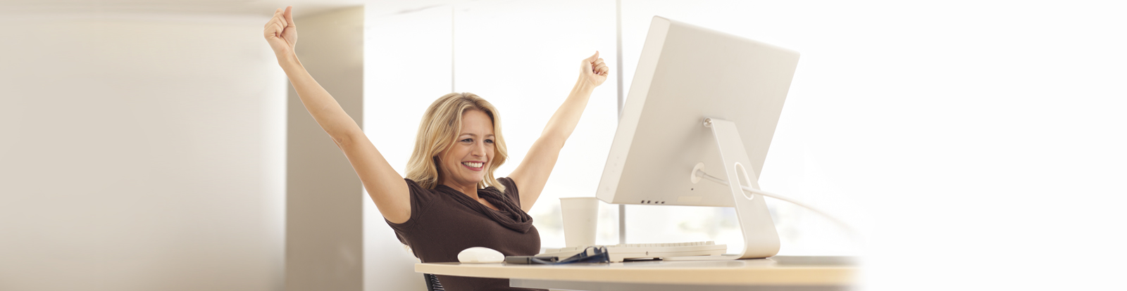 Woman smiling with arms outstretched sitting at laptop in brightly lit room.